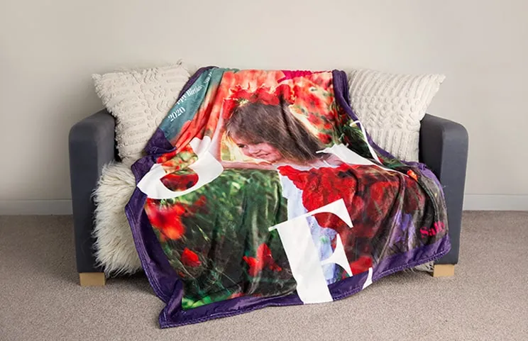Una manta de visón personalizada de Printerpix con un niño sobre ella, colocada sobre un sofá. La palabra "amor" es visible.