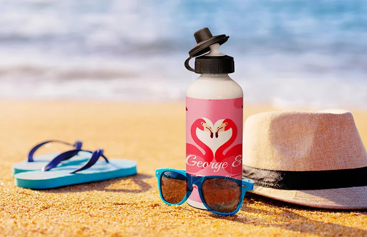 Botella de agua personalizada con flamenco en playa de arena, junto a gafas de sol y sombrero. ¡Regalo de verano perfecto!