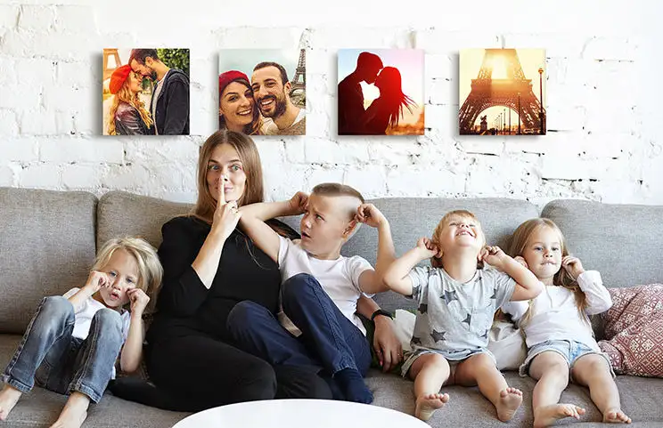 Mamá y cuatro niños pequeños sentados en el sofá frente a cuatro lienzos fotográficos
