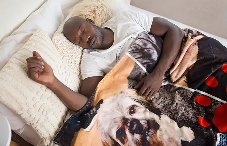 Un hombre duerme en la cama bajo una manta personalizada de Printerpix con diseño de perros.